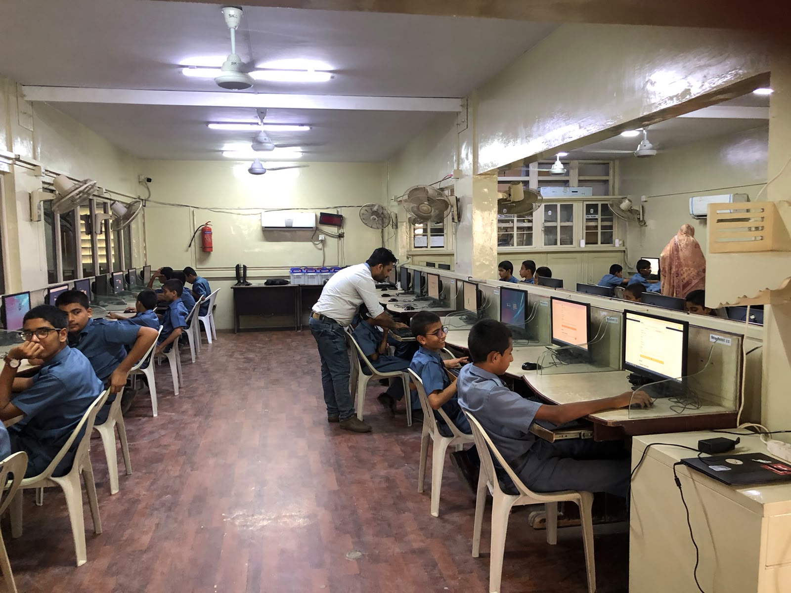 Students working at computers during a ThinkHumanly workshop while a facilitator checks in with them