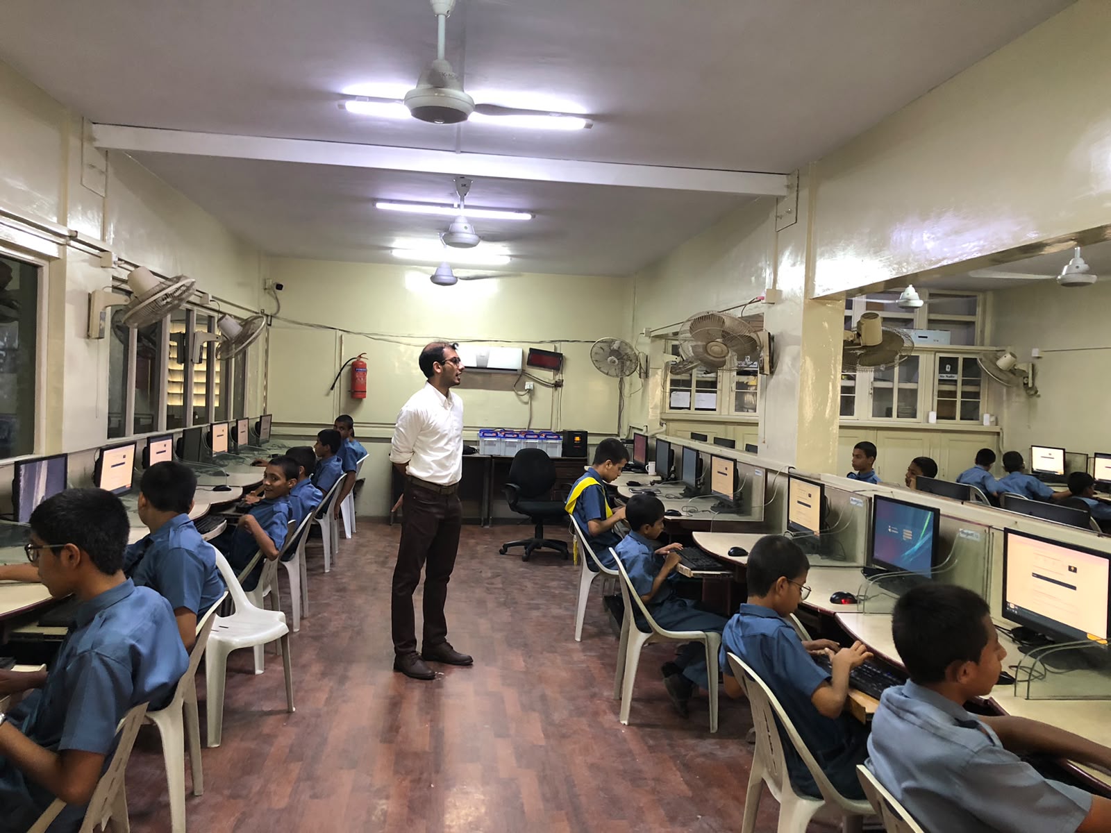 A facilitator guiding a class of students seated at computers in a school lab